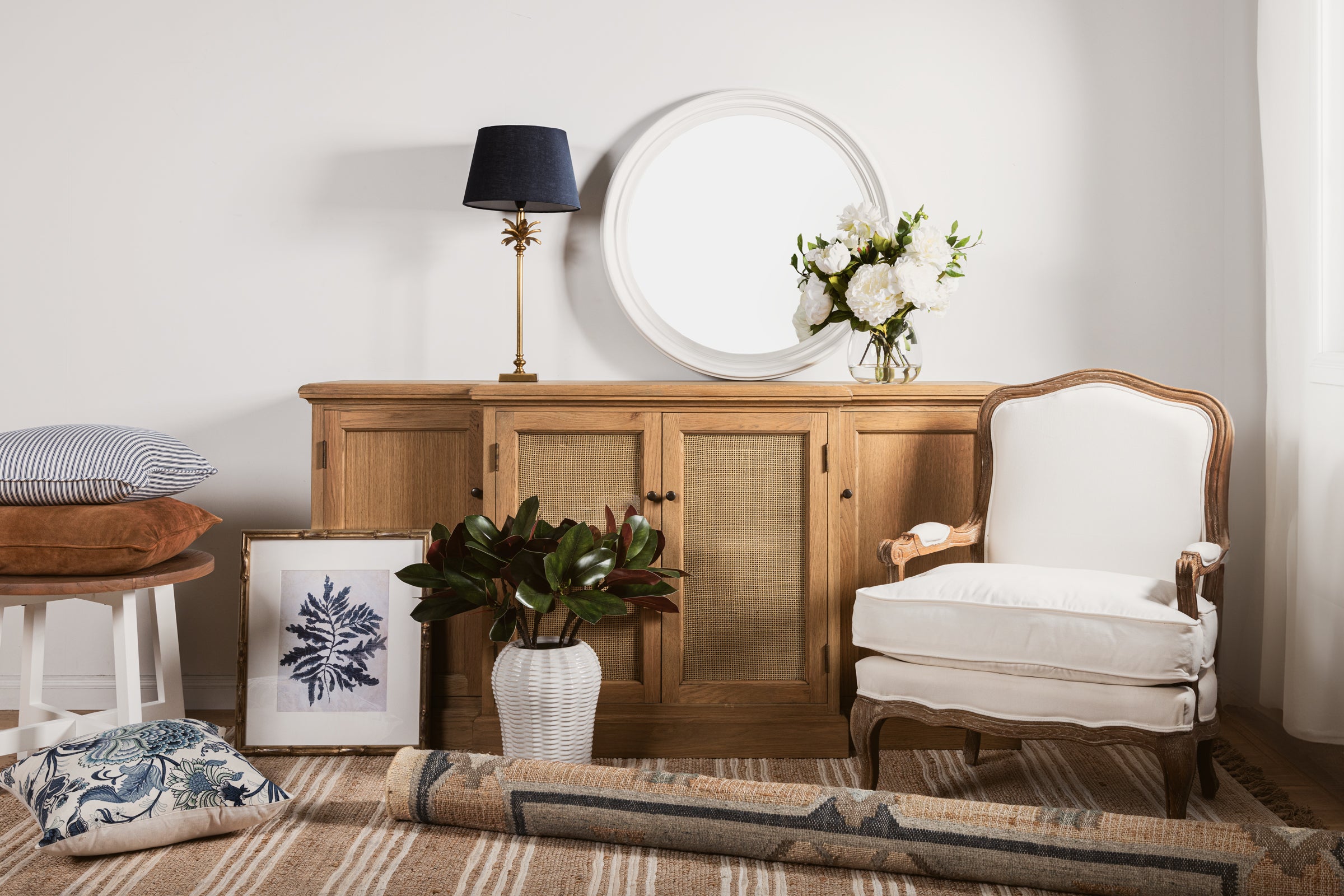 A selection of home décor items including a chair, side board, mirror, lamp and cushions.