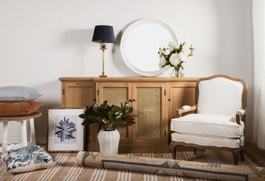 A selection of home décor items including a chair, side board, mirror, lamp and cushions.