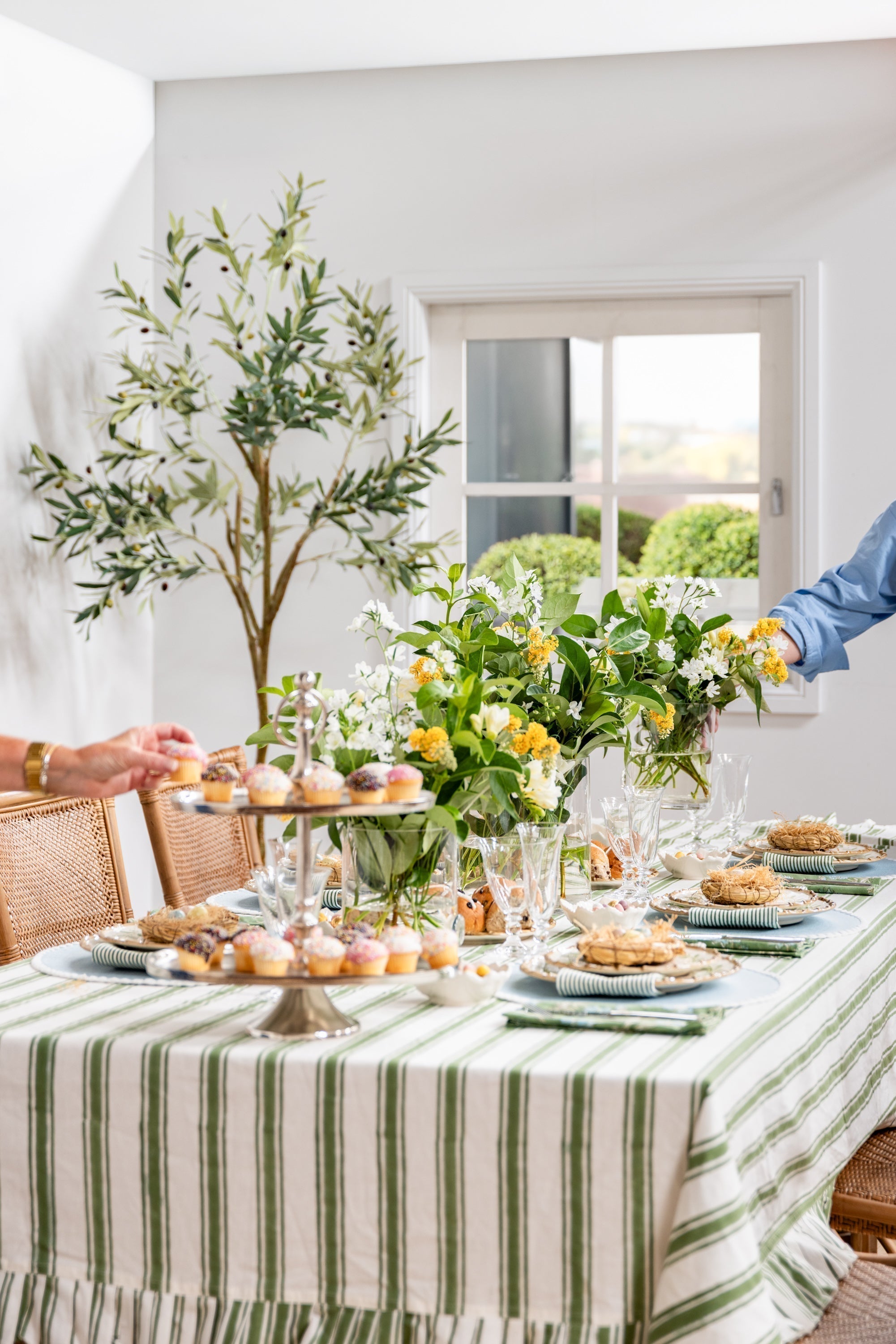 A curated indoor easter dining table with a striped green tablecloth, cohesive colour placemats with a fresh floral arrangement as the centrepiece.