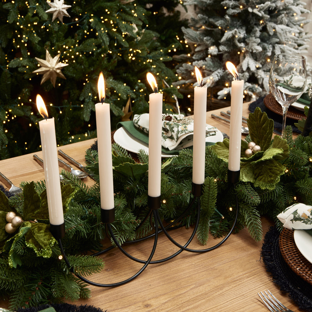 Candles in a black iron candle holder next to a garland on a table.