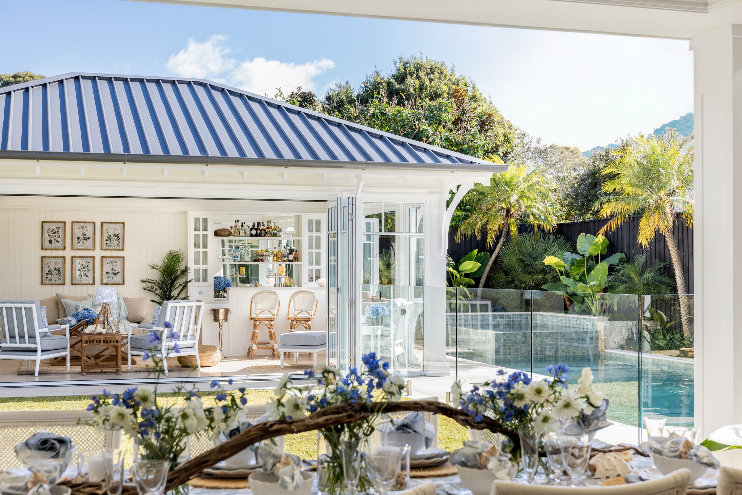 Overview of Coastal Collection Featuring Outdoor Dining Table with Pool house including three Indira Chairs and Indira ottoman and two Antigua bar stools.