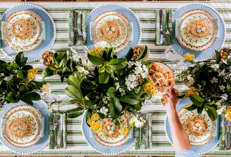 Top-down view of a table set with plates, flowers, and a person holding a plate.