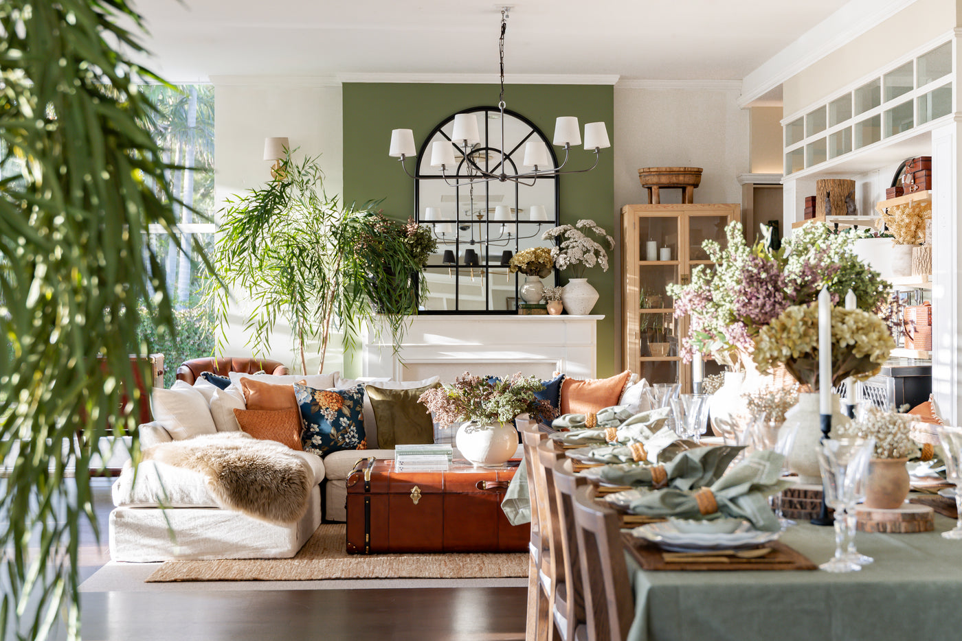 Living room with a fireplace, plants, dining table and lounge with scattered cushions on it.