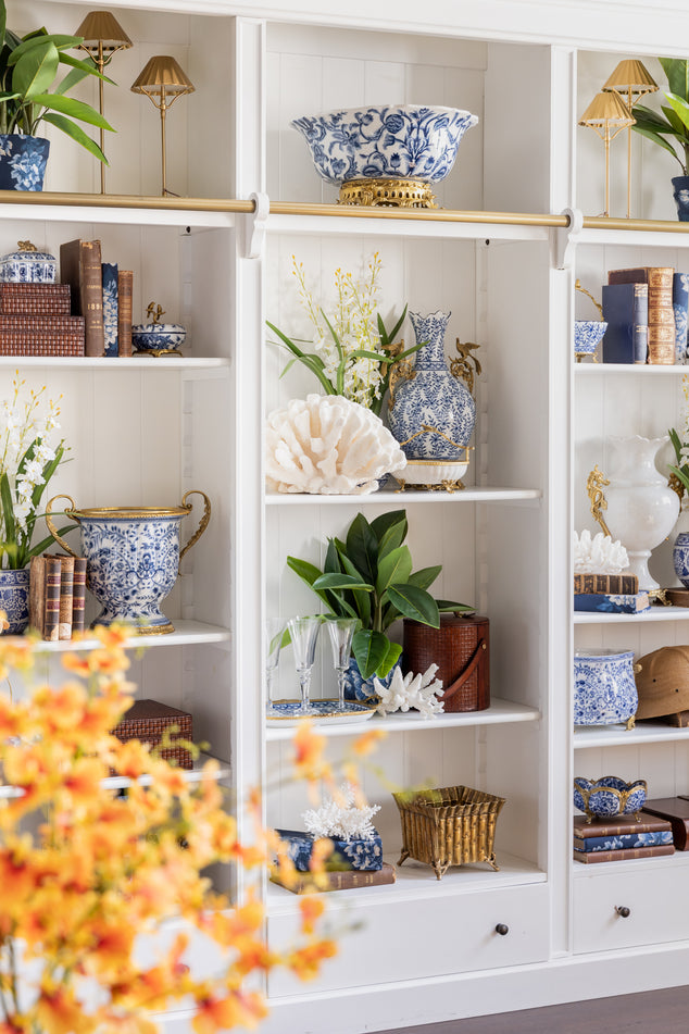 White bookcase styled with blue and white barclay pieces and green flroals