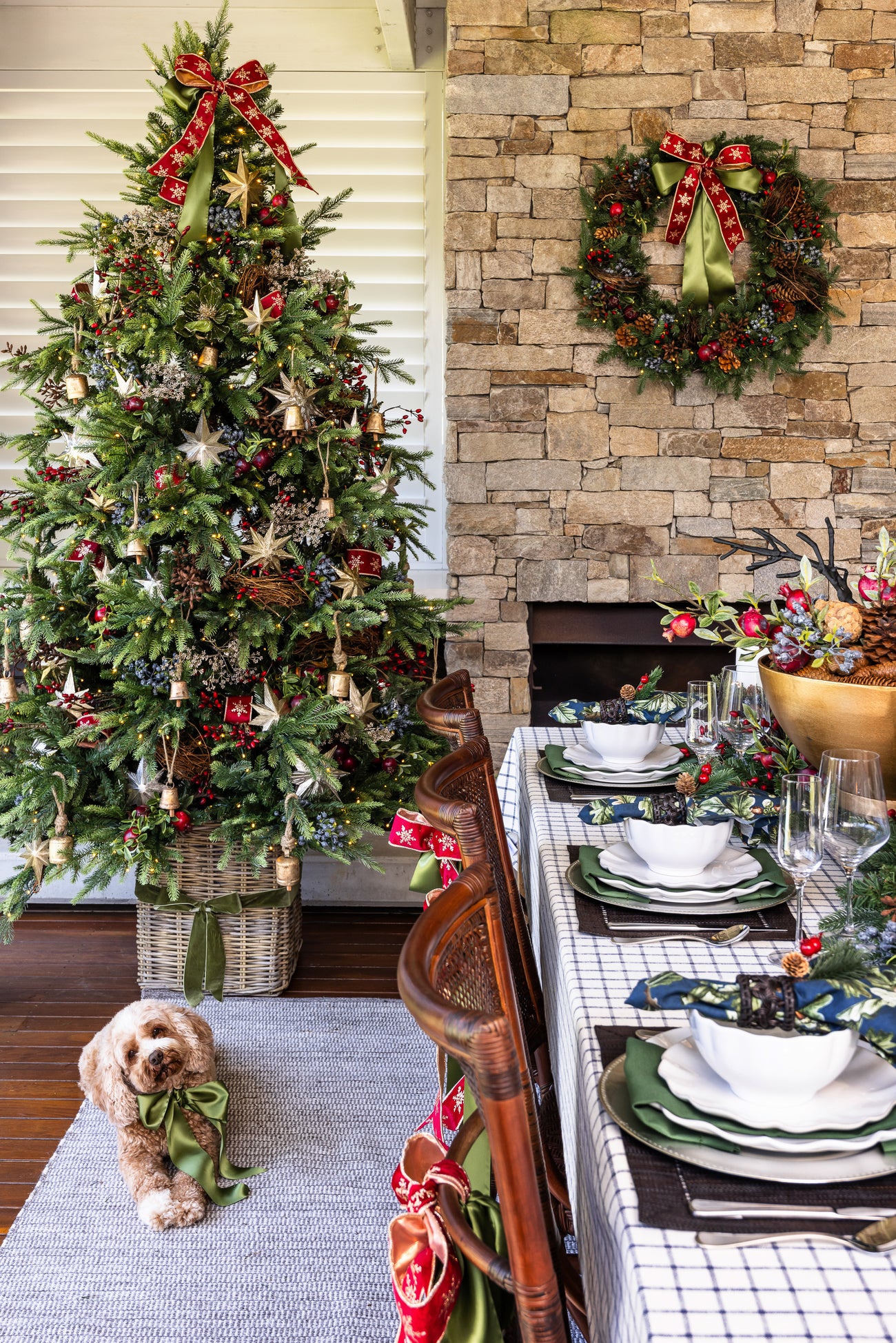 A cute dog sits in front of a Christmas tree decorated in a modern farmhouse style. A dining table set for Christmas day is in the foreground.