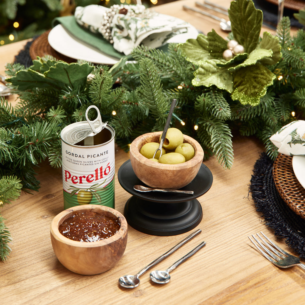 A condiment fork in a bowl of olives near a Christmas garland.