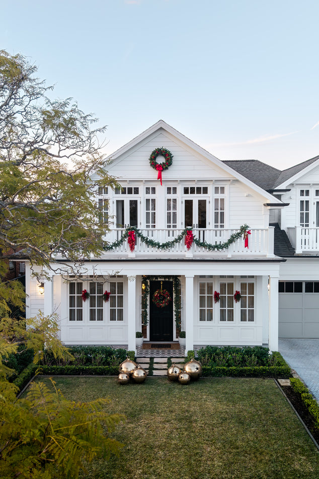 Shot of Front of House decorated for Christmas with Red Magnolia Decor and Oversized Gold Bells on the Front lawn
