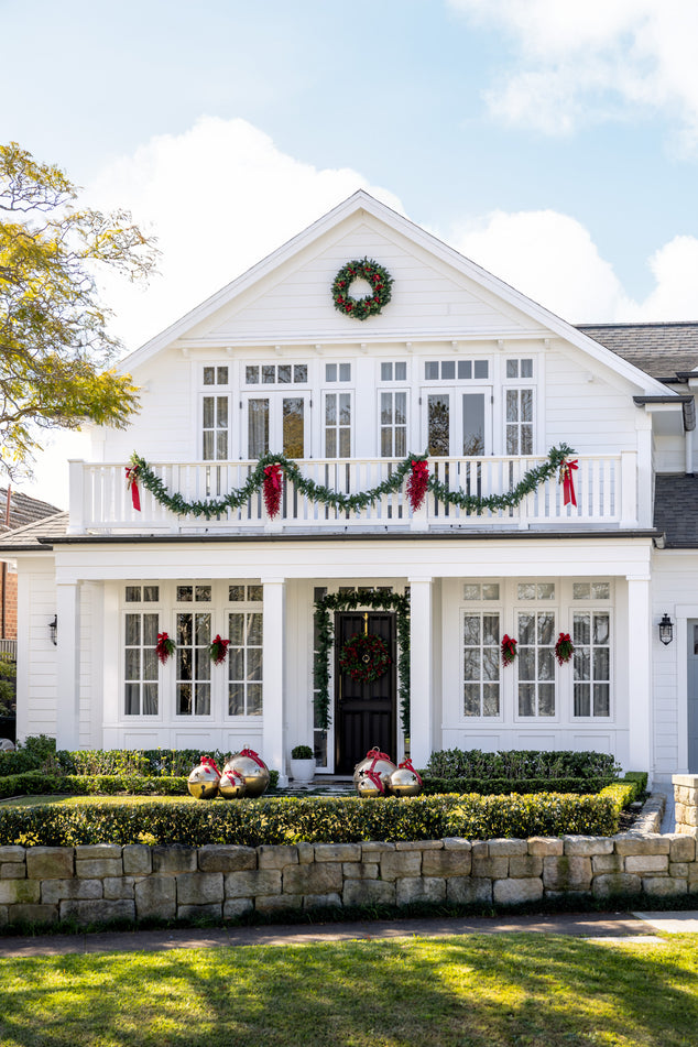 White house decorated with Christmas garlands and wreaths on a clear day.