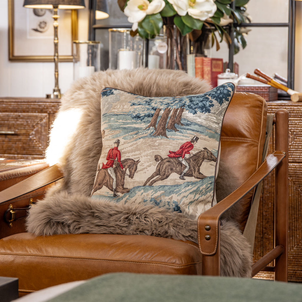 Brown leather armchair with decorative pillow featuring horse and rider design, surrounded by indoor plants.