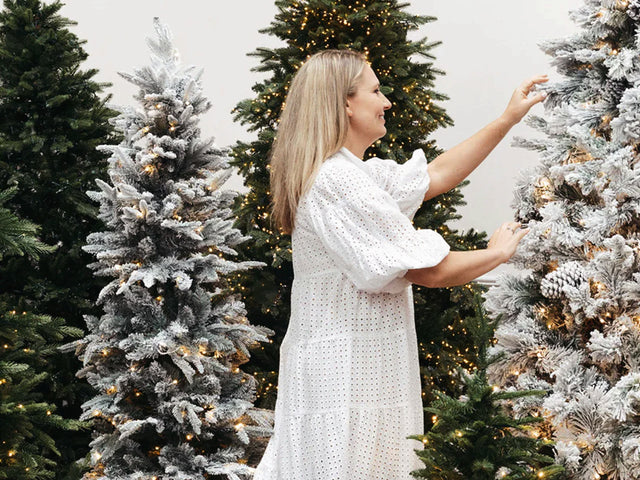 Lady in white dress surrounded by Christmas trees.