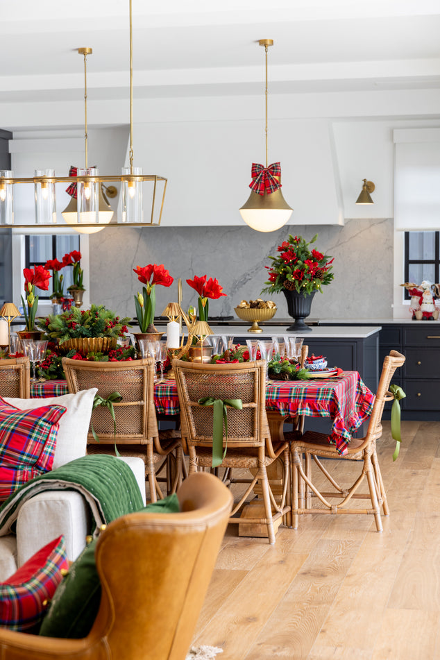 Dining room with a table set for Christmas, decorated with red and green tableware, chairs, and flowers.