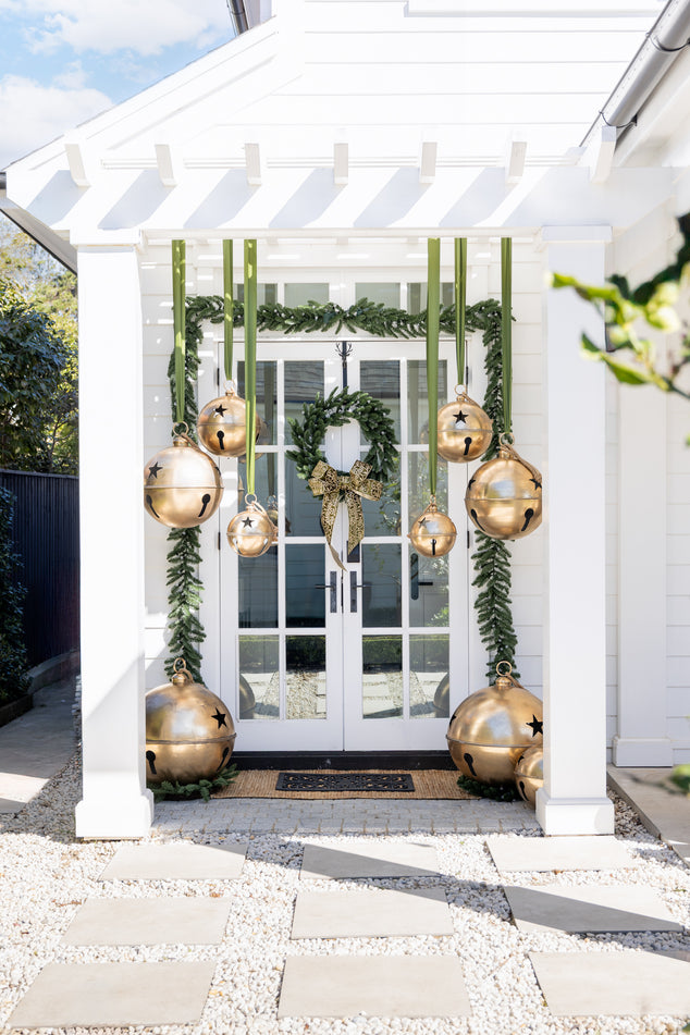 Laundry Door Decorated with Green Garland and Wreath and Oversized Gold Bells Hanging from Pergola