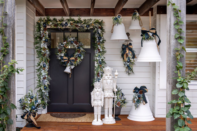 A front porch styled with giant white bells, blueberry garlands, wreaths and large white nutcrackers.
