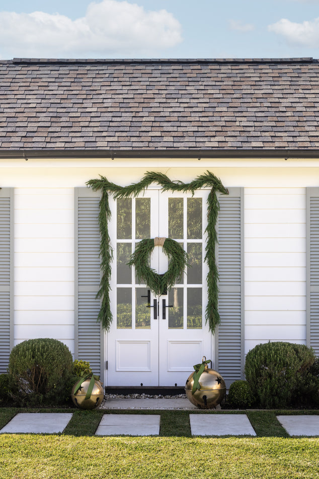 Pool house Door Styled with Norfolk Garland and Wreath with Over sized Gold Bells placed in front