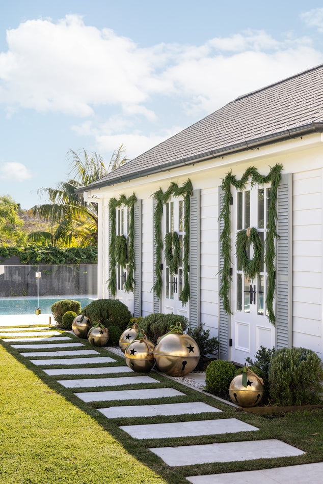 Pool house with Norfolk Garlands and Wreaths on the Doors and Gold Oversized Bells placed in front