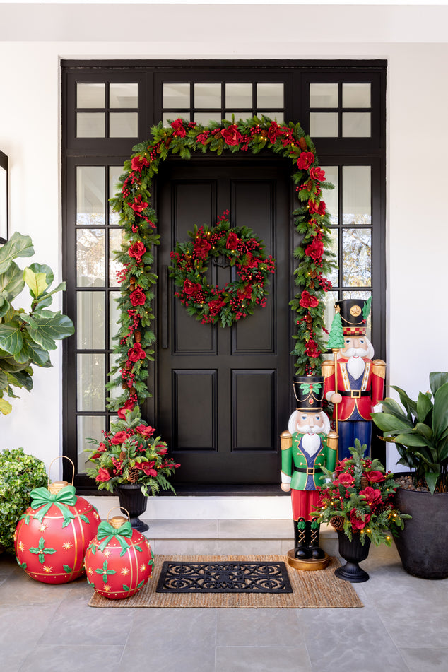 Christmas Door Styled with Red and Green Garland and Wreath with Oversized Baubles and Nutcrackers in Front of Door