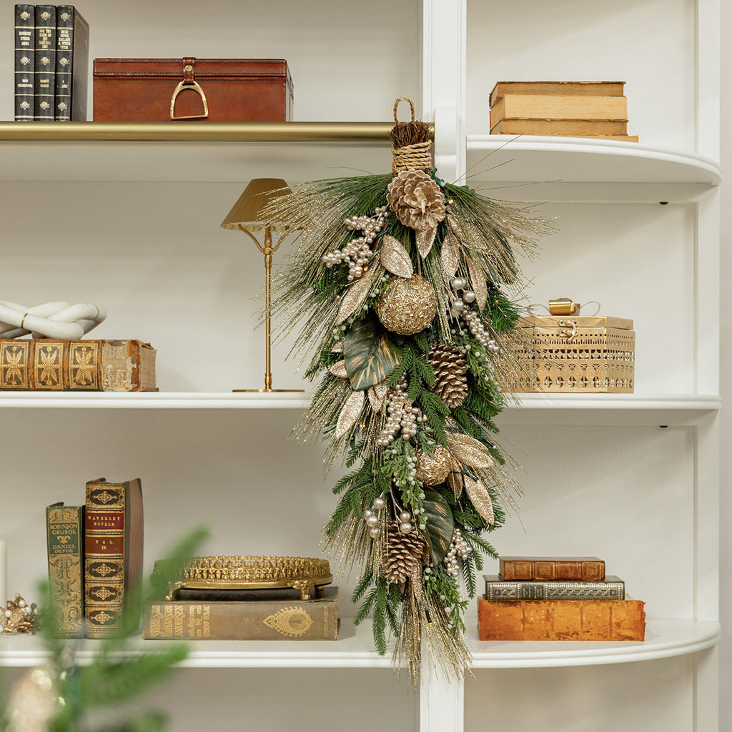 A mixed metal Christmas teardrop decoration on a bookshelf.