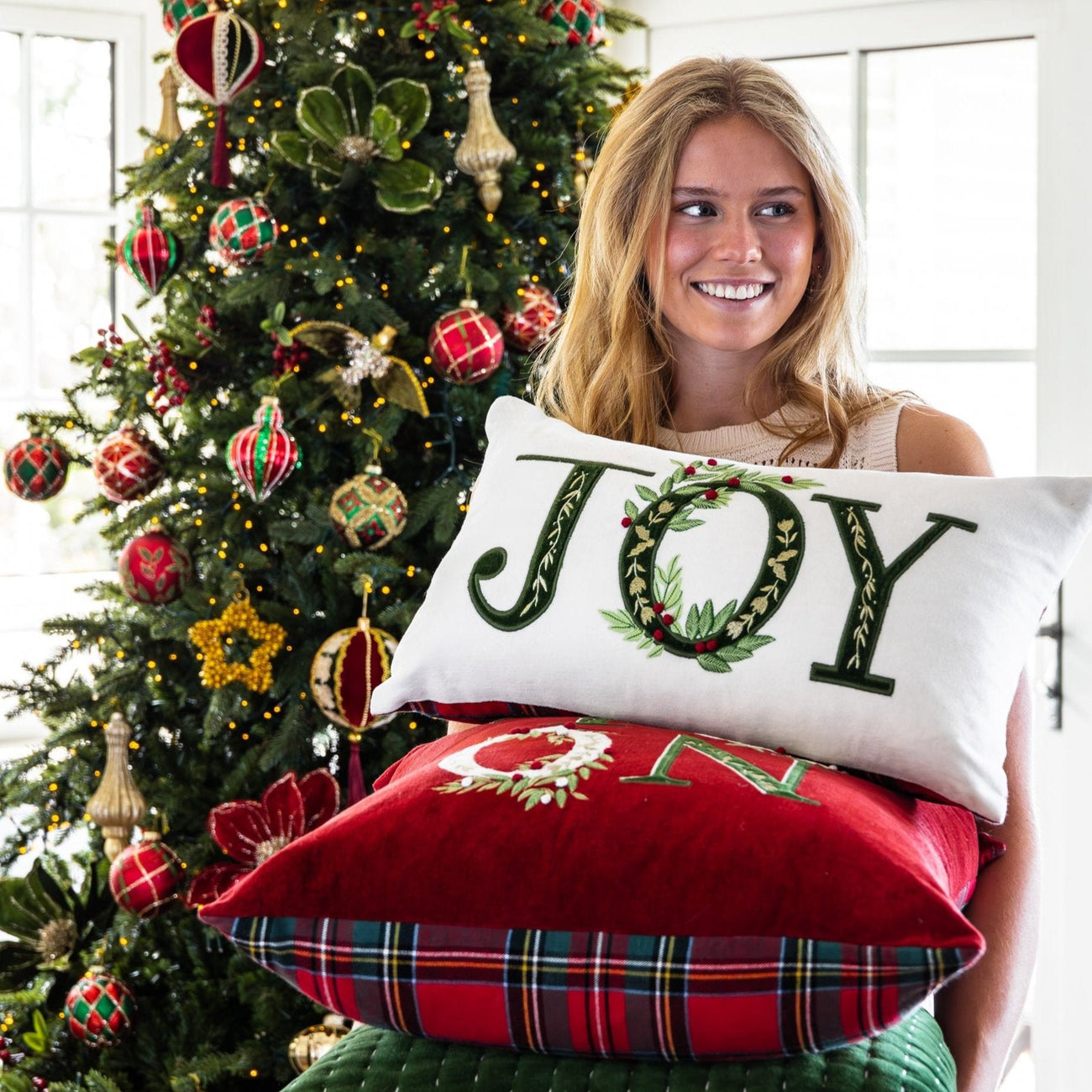 Grace holds a stack of velvet Christmas cushions in front of a Christmas tree.