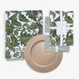 Green and gold damask patterned napkin and tablecloth, a green and white striped napkin, and a round woven-look gold placemat.