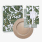 Green and gold damask patterned napkin and tablecloth, a green and white striped napkin, and a round woven-look gold placemat.