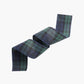 A rolled piece of tartan plaid fabric in green and blue, shown on a plain light gray background.