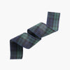 A rolled piece of tartan plaid fabric in green and blue, shown on a plain light gray background.