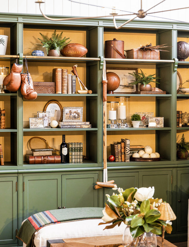 Green bookshelf with eclectic decorative items featuring leather and rattan accents.