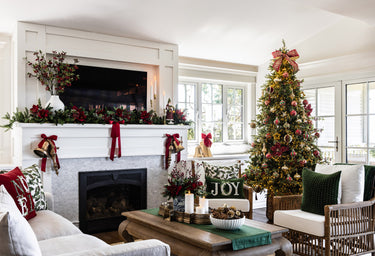 A Christmas living room with a green table runner, candles, amaryllis sprays, and velvet cushions.