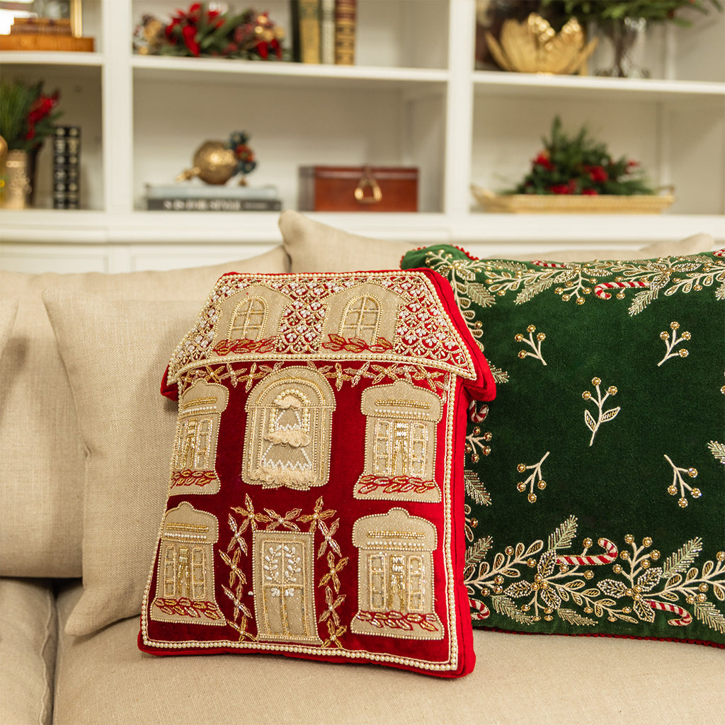 A red beaded Christmas house cushion on a lounge next to a green velvet cushion.