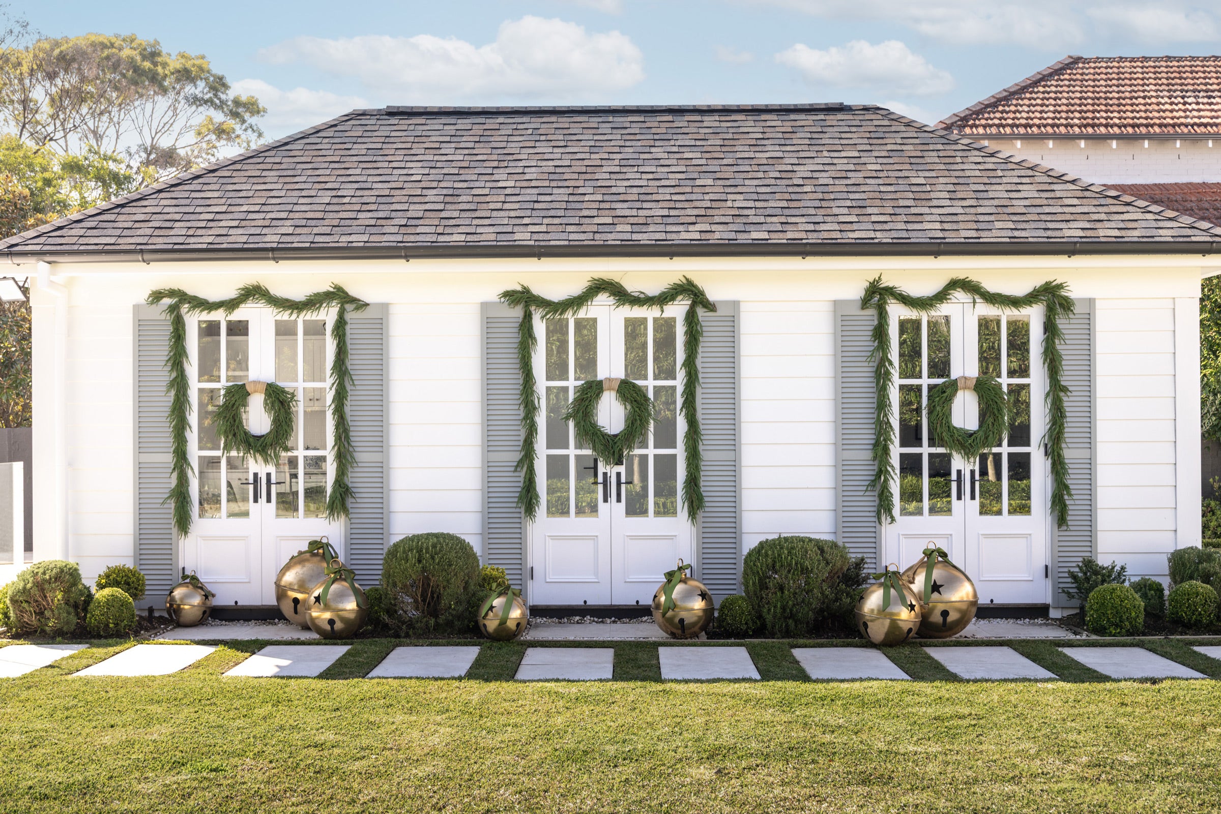 Green wreaths & garlands on a pool house with giant gold bell decorations.