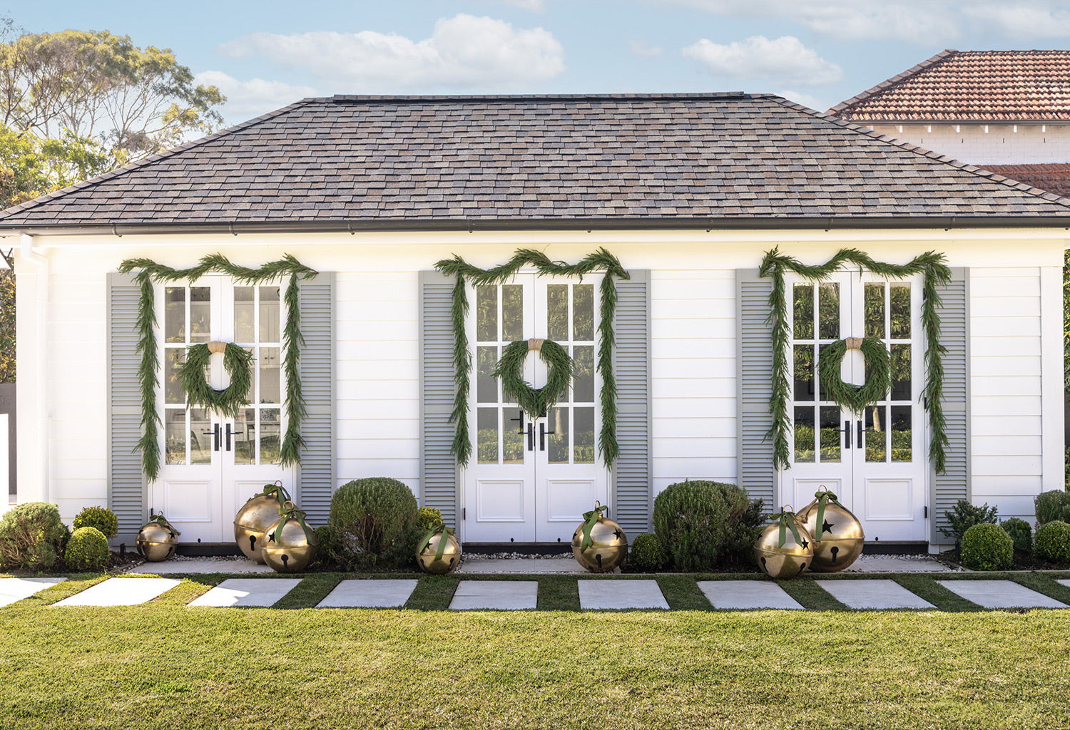 Green wreaths & garlands on a pool house with giant gold bell decorations.