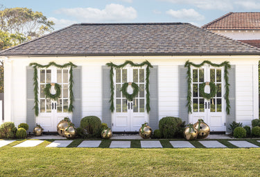 Green wreaths & garlands on a pool house with giant gold bell decorations.