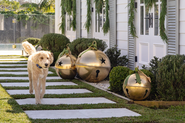 Dog is walking past giant gold bells outside white pool house.