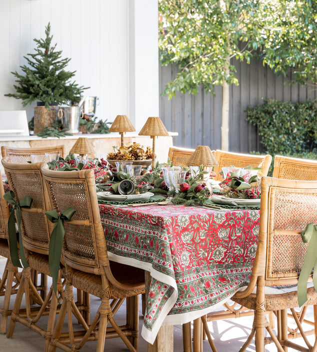 Dining table set for Christmas with a patterned red & green tablecloth.