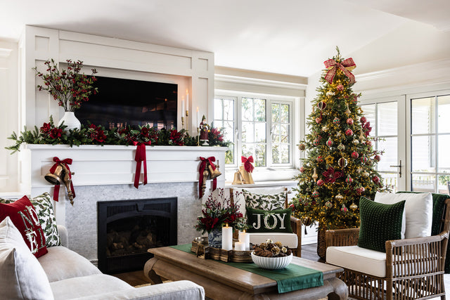 A living room setup for Christmas with a Christmas tree styled with red, green and gold baubles. A mantel displays an amaryllis garland and Christmas cushions are on the lounge.