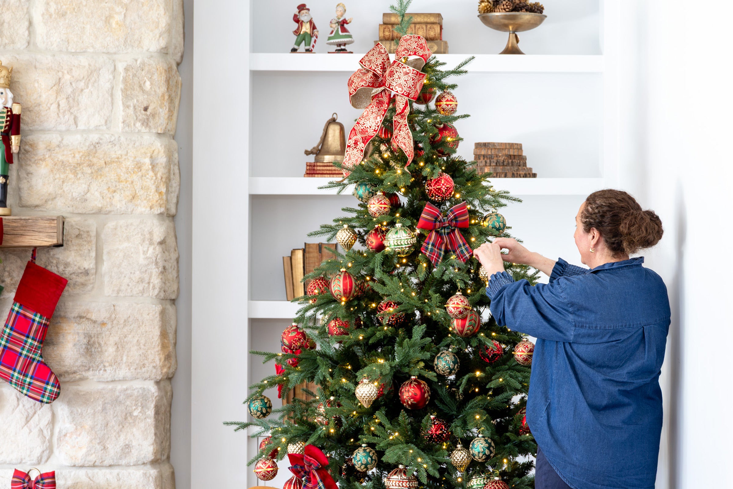 Lady decorating a Christmas tree with red and green glass baubles. 