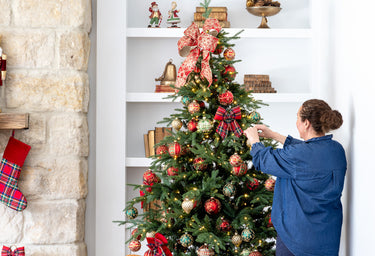 Lady decorating a Christmas tree with red and green glass baubles. 