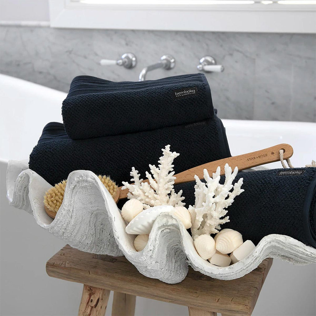 Large white clam shell bowl beside a bath holding towels and a brush