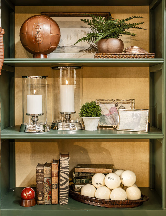 Decorative shelf with books, candles, leather soccer ball, cricket and polo balls.
