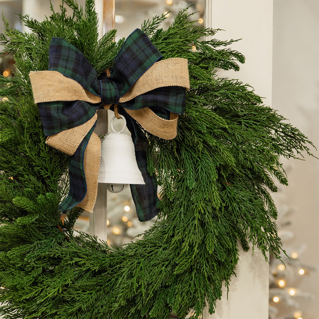 Green wreath decorated with tartan and hessian ribbon and a white bell.