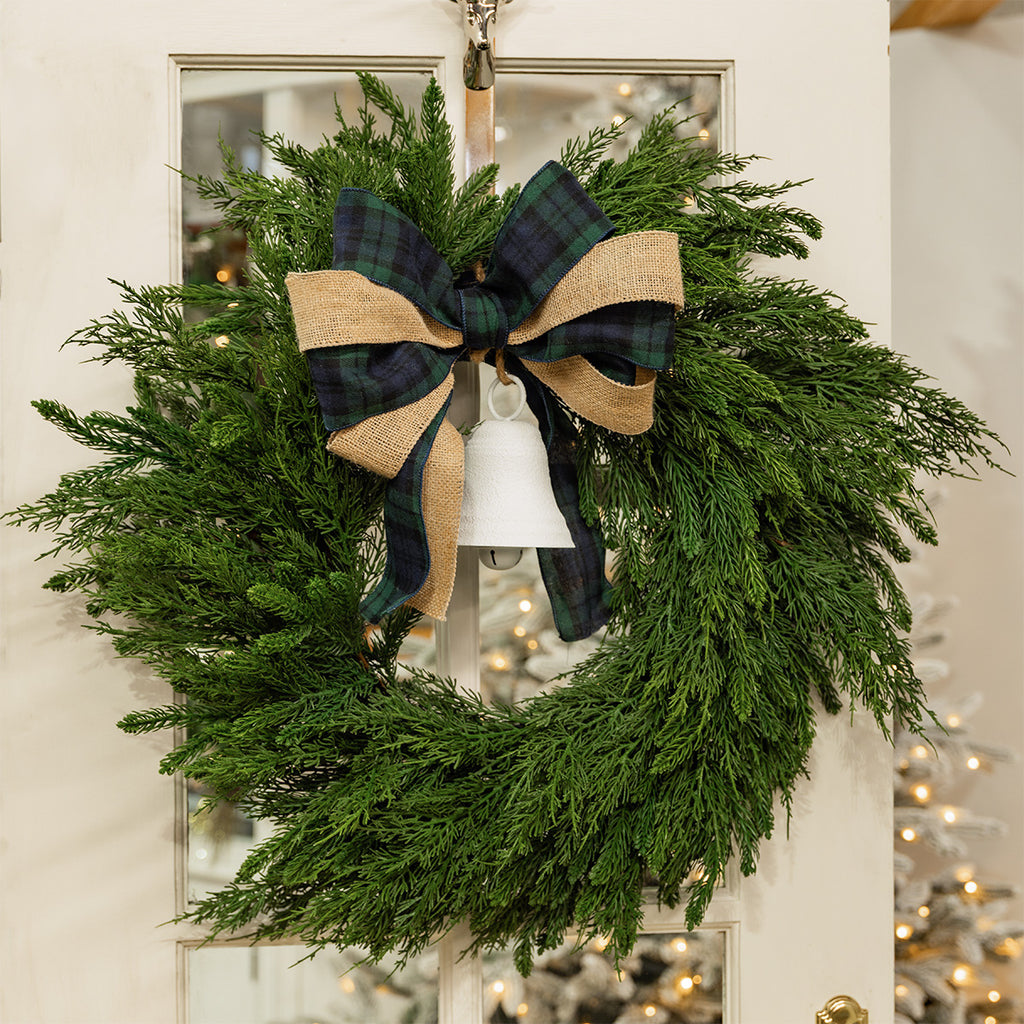 Green wreath decorated with tartan and hessian ribbon and a white bell.