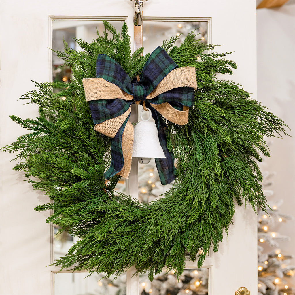 Green wreath decorated with tartan and hessian ribbon and a white bell.