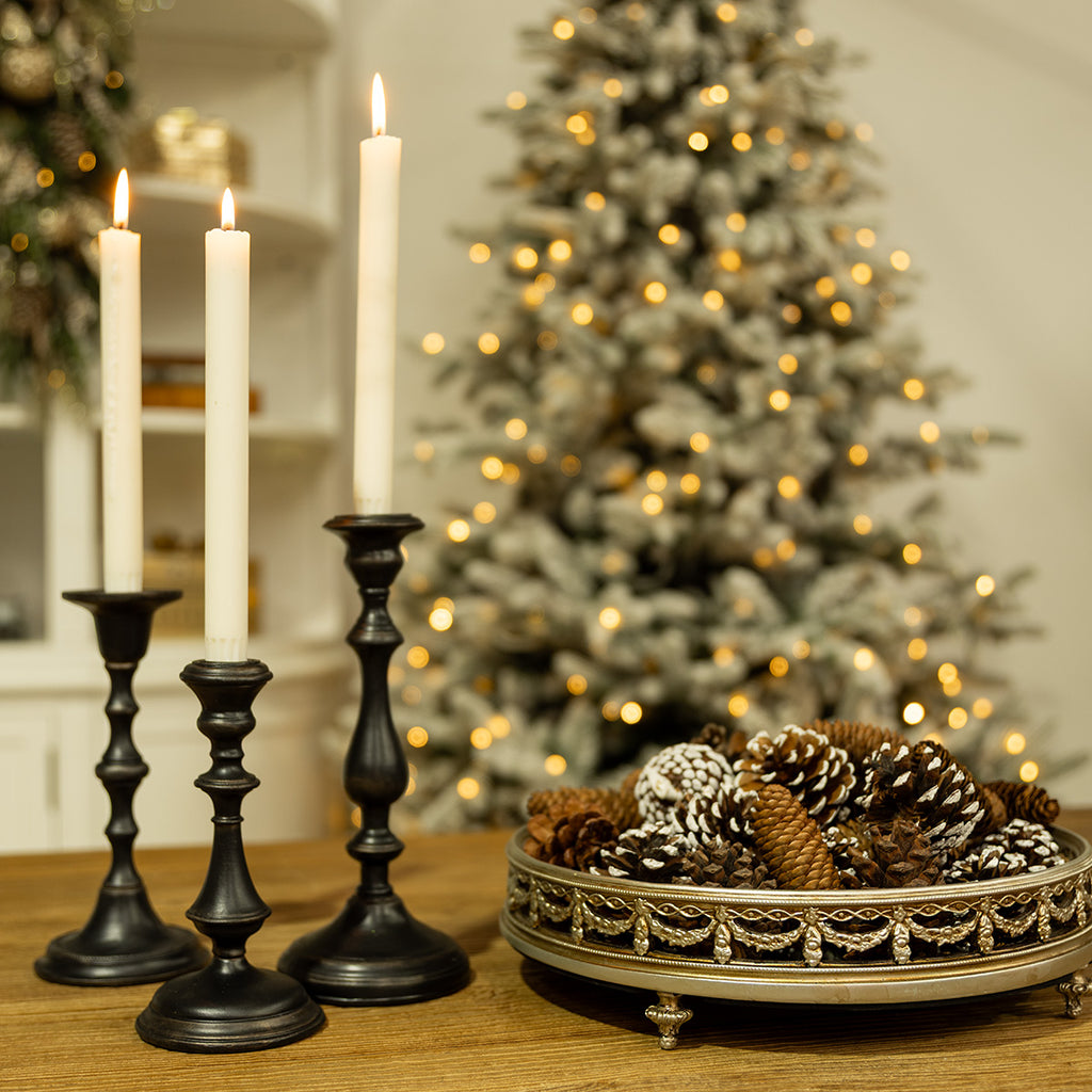 Three candle holders with white candles on a table.