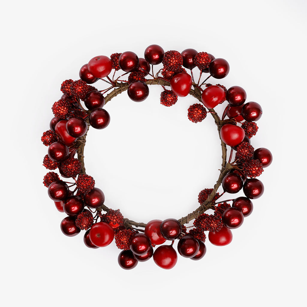Top view of a decorative holiday candle wreath made of red berries and glossy red ornaments on a white background.