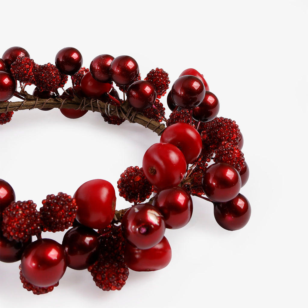 Close up: A decorative holiday candle wreath made of red berries and glossy red ornaments on a white background.