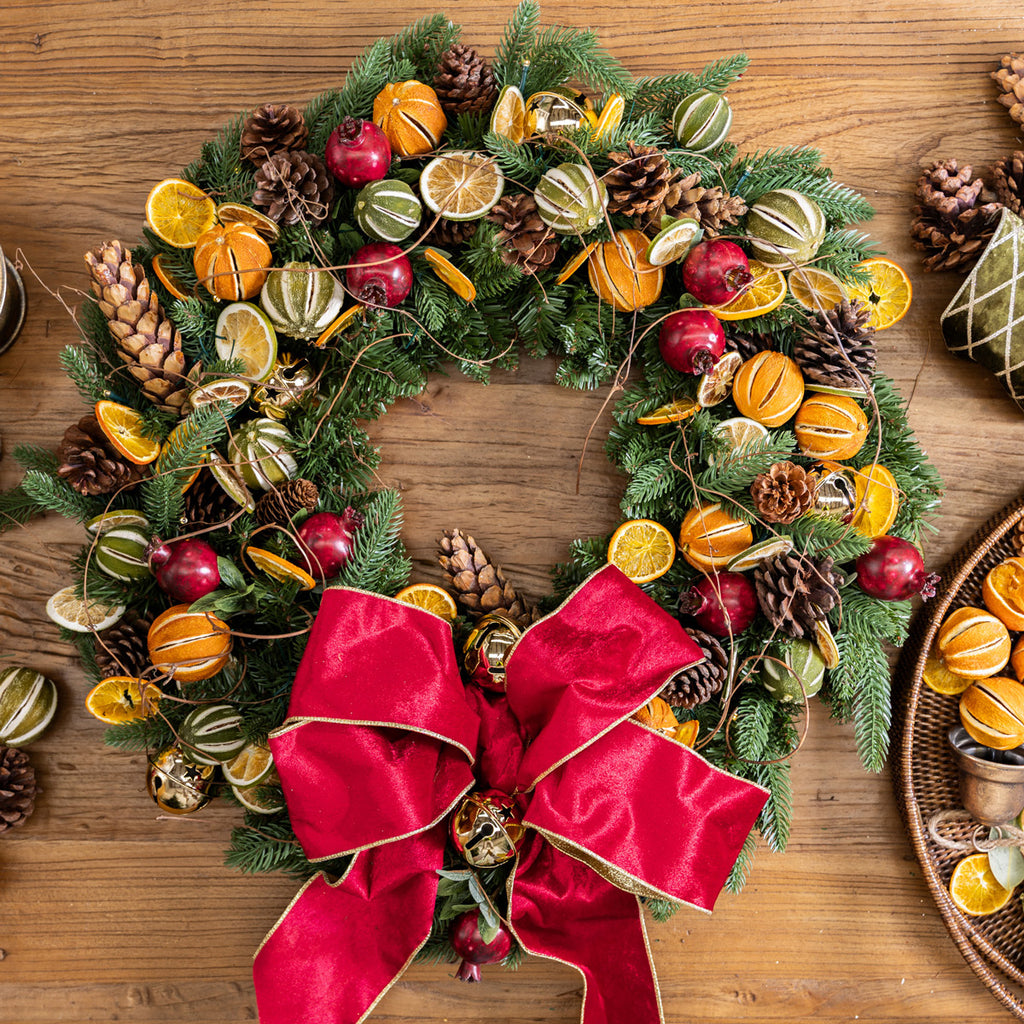 Decorative Christmas wreath with fruits and a red bow on a wooden surface