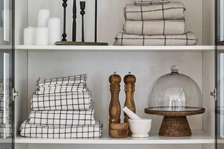 A stack of blue and natural check tablecloths & napery on a shelf.