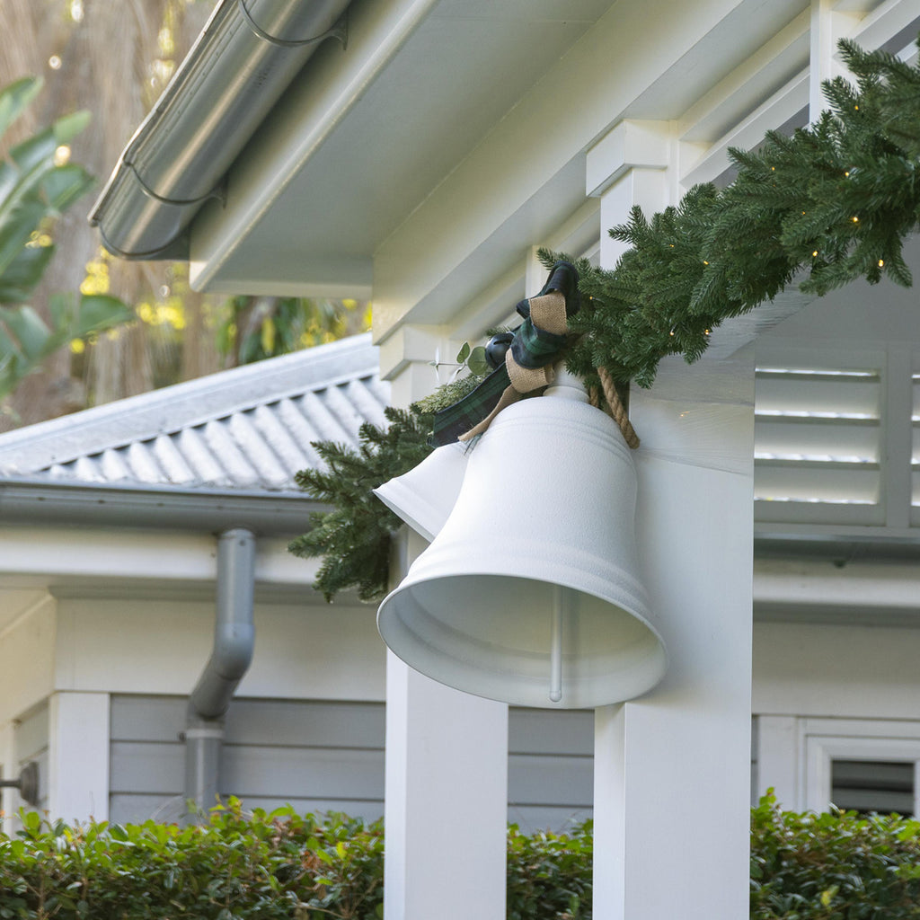 White bells with green garland hanging on a house.