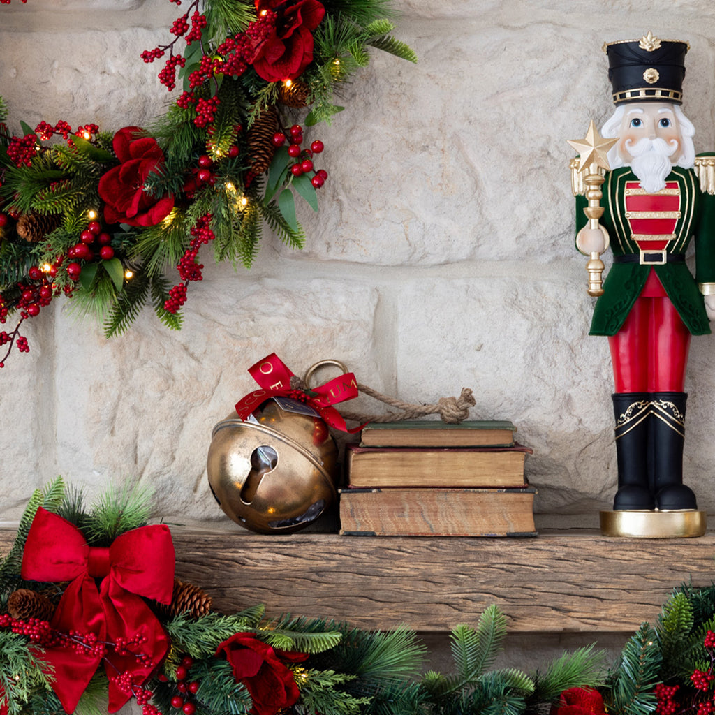 Decorative Christmas mantel with a nutcracker, books, bell, and garland.