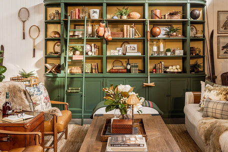 Living room with a large green bookshelf filled with decorative items, a wooden coffee table, and leather armchairs.